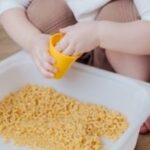 toddler playing in macaroni
