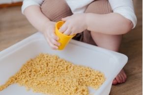 toddler playing in macaroni